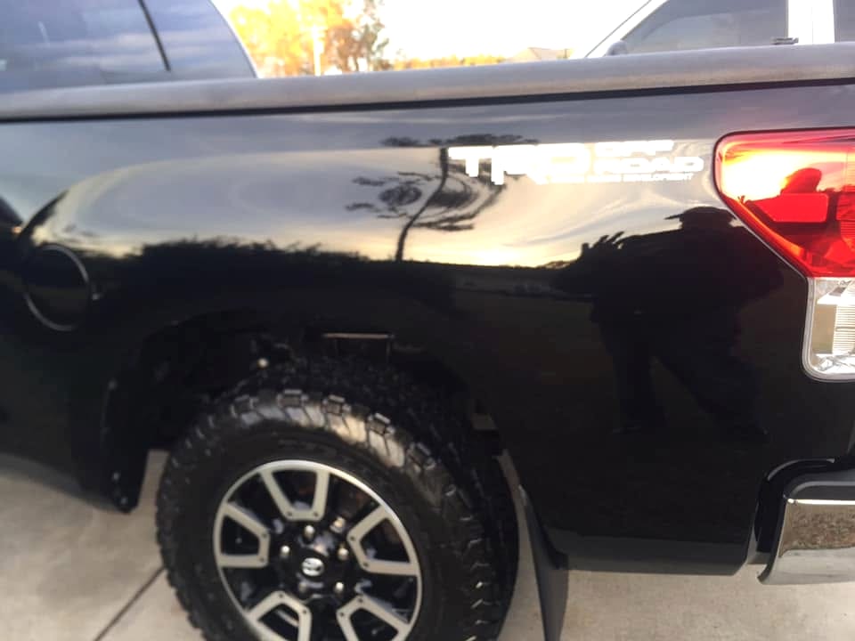 Reflection of a detailer at work in the mirror-finish black paint of a freshly corrected truck